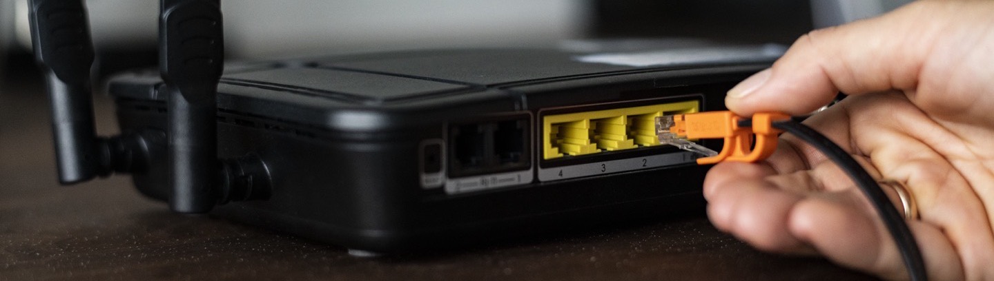 A hand pushing an Ethernet cable into the back of a home router.
