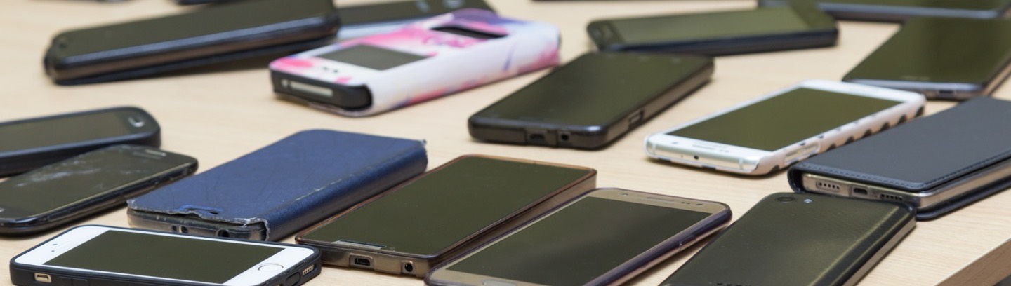 Two rows of retired smartphones laid out on a table, screens off.